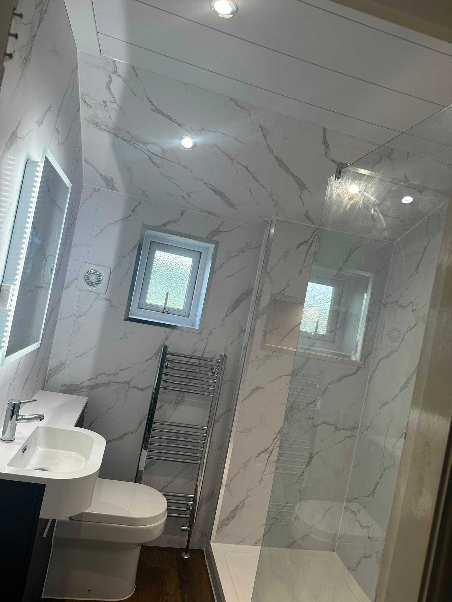 Completed bathroom electrical work — recessed lighting, extractor fan and shaver socket in a marble-tiled bathroom